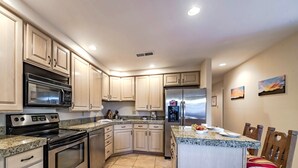 A modern kitchen with stainless steel appliances, light wood cabinets, a granite countertop, and a breakfast bar with chairs. - DB Mountain by Ruidoso Vacation Rentals (Ruidoso)