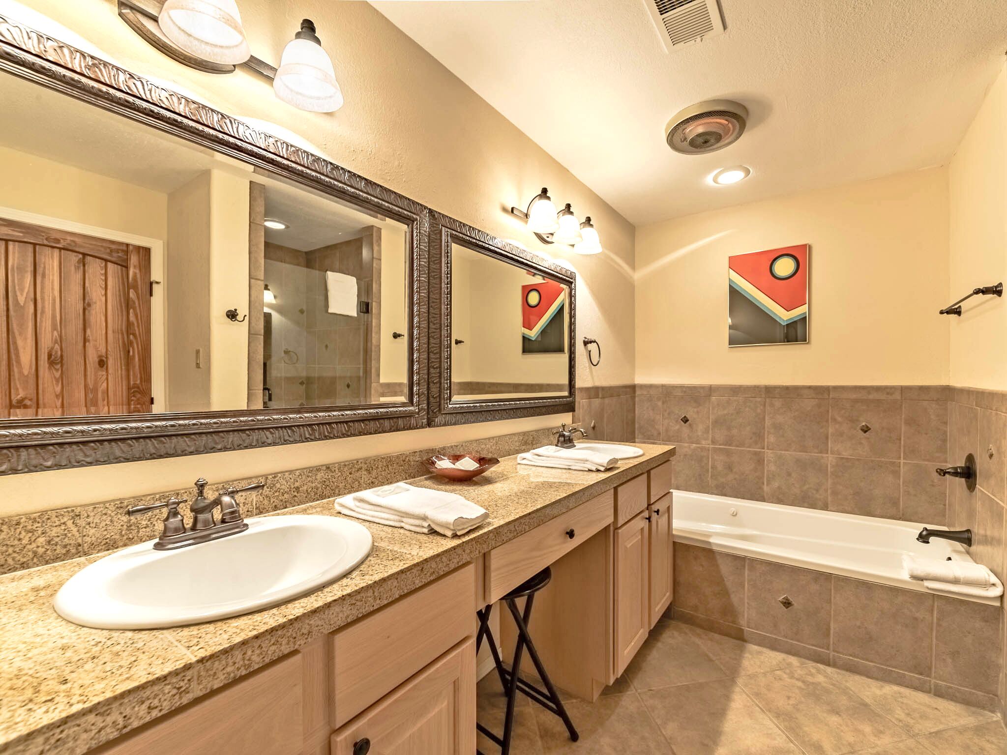 A bathroom with a double sink, a large mirror, a bathtub, and a towel rack.