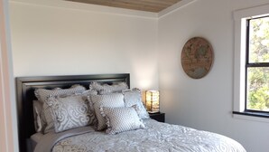 A bedroom with a bed, a ceiling fan, a nightstand with a lamp, a world map on the wall, and a window with a view of trees. - Absolute Repose - Secluded Cottage (Stonewall)