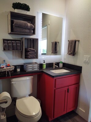 A bathroom with a white toilet, red cabinets, a black countertop, and a mirror with lights. - Absolute Repose - Secluded Cottage (Stonewall)