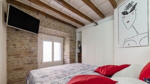 Um quarto com parede de tijolos, vigas de madeira, cama com roupa de cama vermelha e branca, uma janela e um quadro na parede.