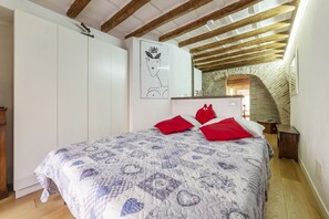 Une chambre à coucher avec un lit, une armoire, un oreiller rouge, un tableau encadré accroché au mur et un plafond en bois.