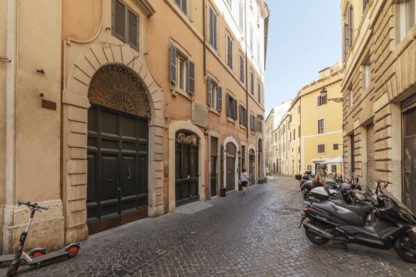 A cobblestone street lined with historic buildings, a scooter parked on the left, and a motorcycle on the right.