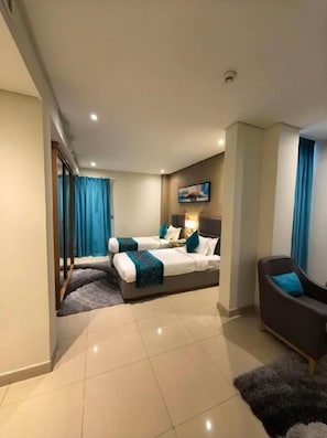 A hotel room with a bed, a sofa, a TV, and a window with curtains. - Meshal Hotel And Spa (Manama)