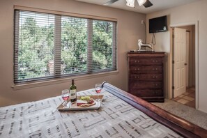 Quarto com cama, cômoda, televisão e janela com persianas.