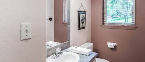 A bathroom with a white sink, a mirror, a toilet, and a window with blinds.
