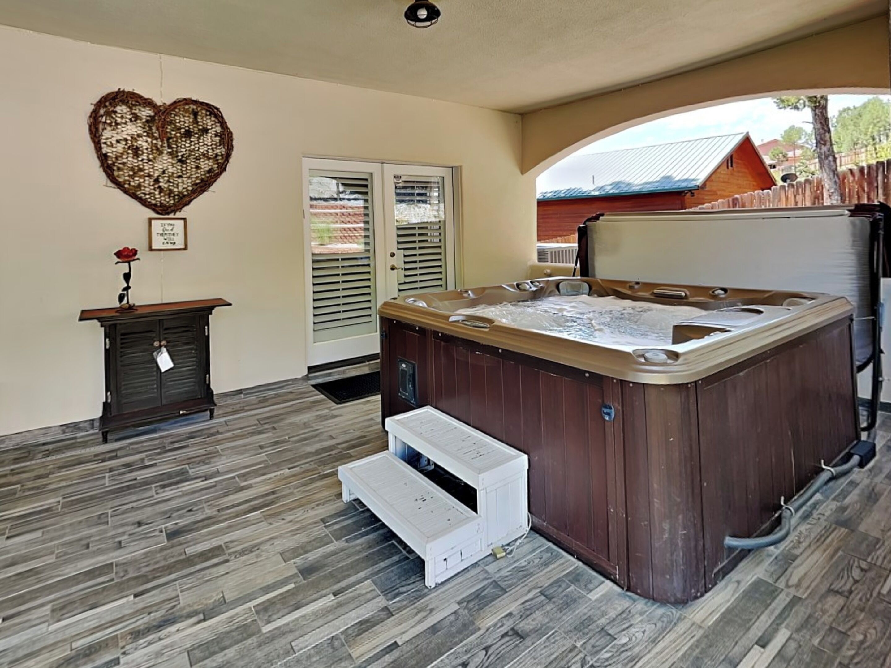 Ein Whirlpool in einem Raum mit Holzboden, einer herzförmigen Wanddekoration und Blick auf ein Haus durch eine Glastür.