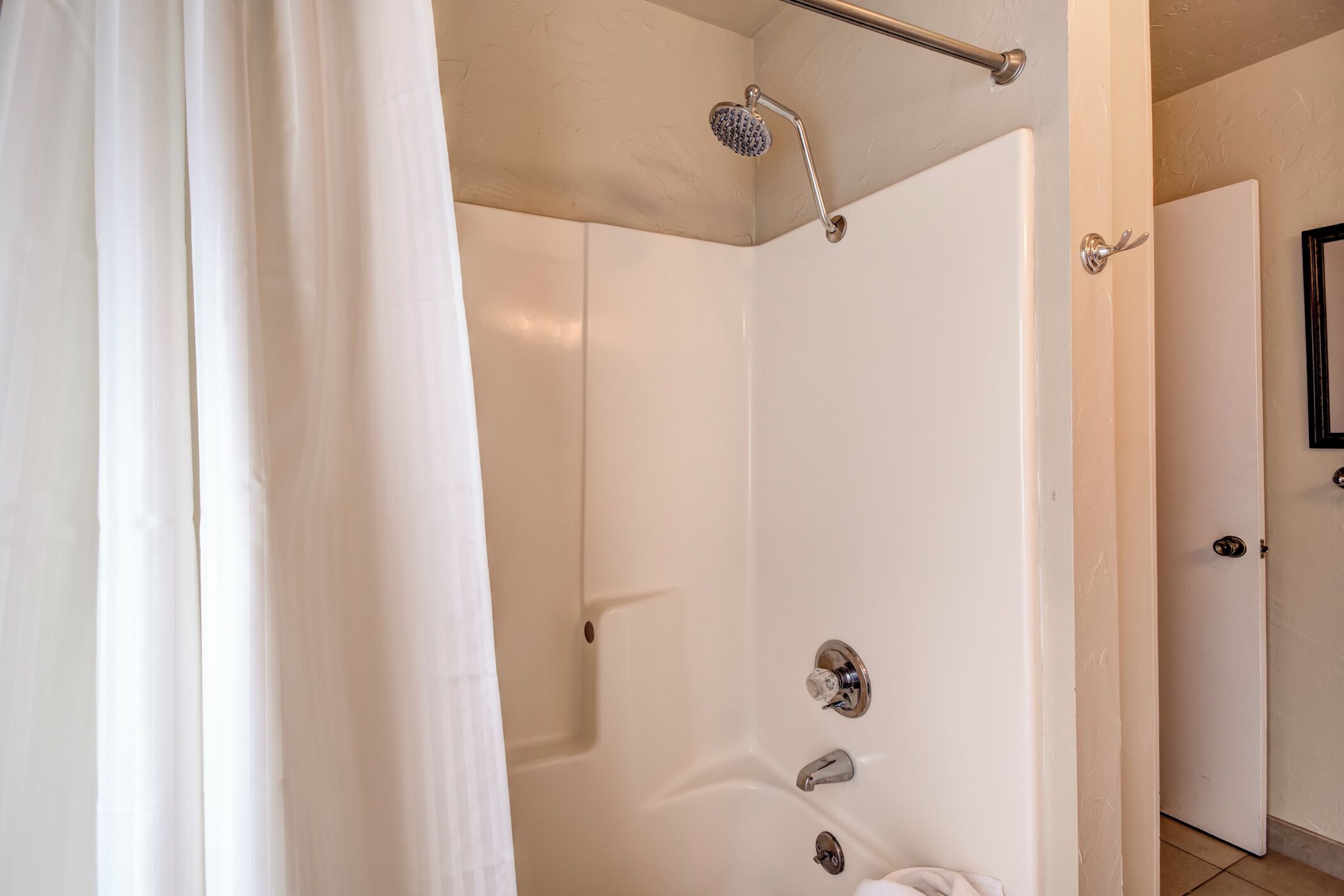 A modern bathroom with a walk-in shower, a towel rack, and a door leading to another room.