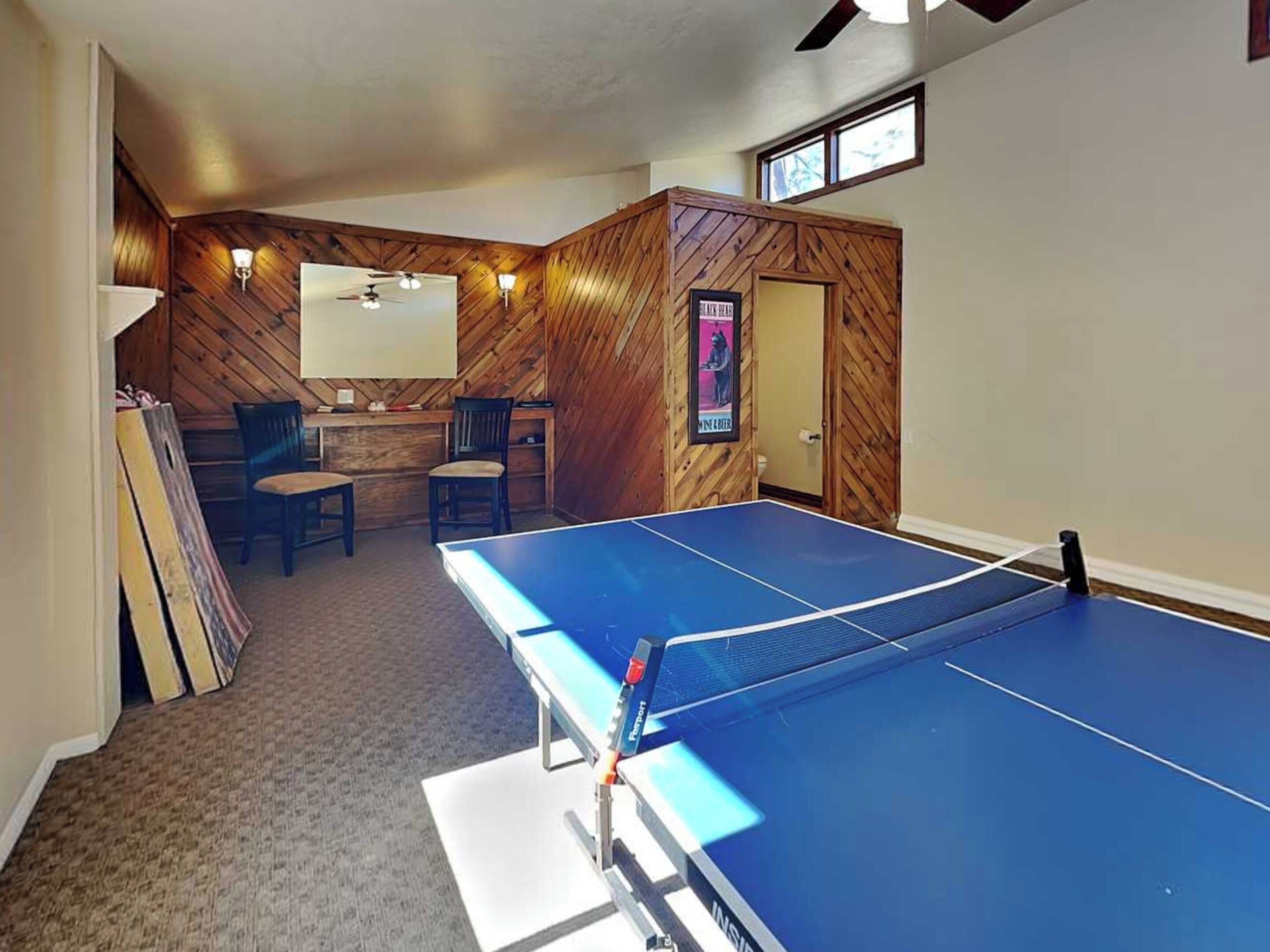 A ping pong table in a room with wooden walls and a ceiling fan.