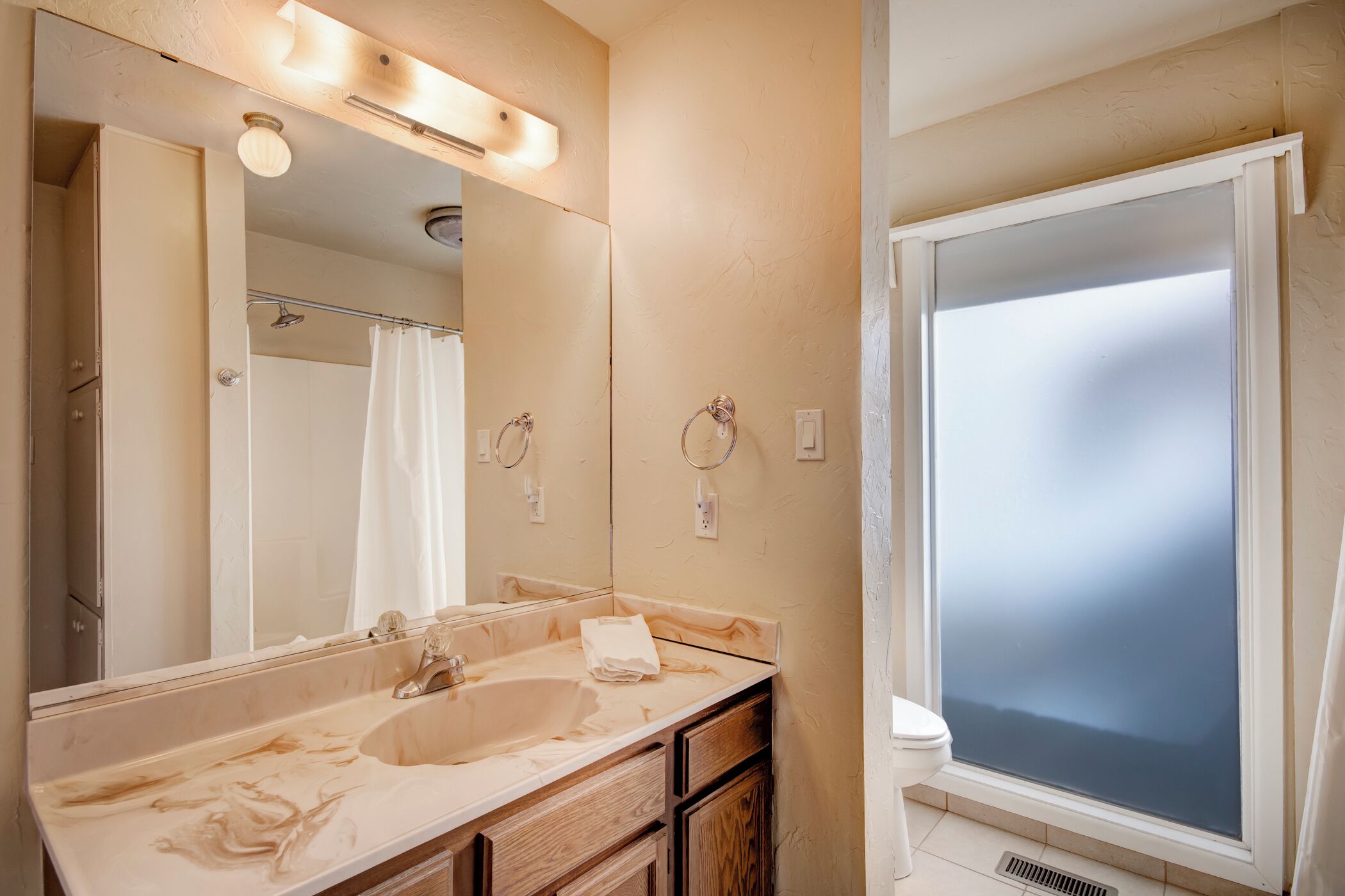 A bathroom with a large mirror, a sink, a toilet, and a shower.