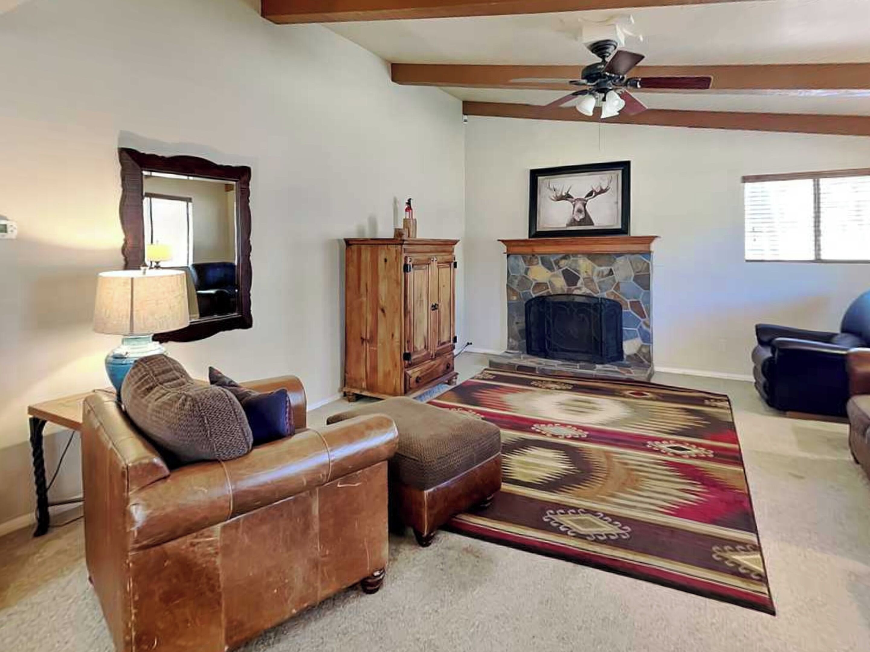 A living room with a leather sofa, a wooden cabinet, a fireplace, and a ceiling fan.