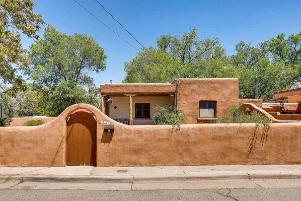 A stucco building with a wooden gate, a small porch, and a window. - Gomez Gardens by Kokopelli Property Management (Santa Fe)