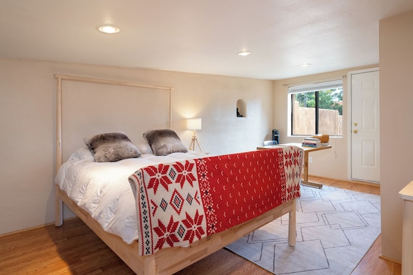 A bedroom with a bed, a bedside table, a lamp, and a window. - Gomez Gardens by Kokopelli Property Management (Santa Fe)