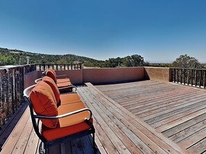 A wooden deck with outdoor seating, a stone wall, and a view of a hilly landscape. - Moonstar by Kokopelli Property Management (Santa Fe)