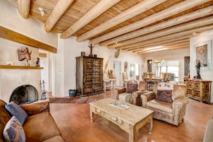 A rustic living room with exposed wooden beams, a fireplace, leather sofas, and a traditional cabinet.