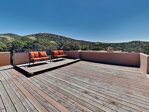A wooden deck with two orange sofas and a table, overlooking a hilly landscape. - Moonstar by Kokopelli Property Management (Santa Fe)