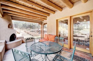 An outdoor patio with a round metal table and chairs, a stone fireplace, and a view of a landscaped garden.