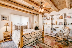 A cozy bedroom with a wooden bed, a fireplace, a bookshelf, and a rocking chair.
