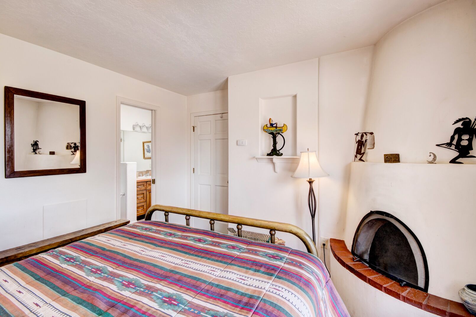 A bedroom with a bed, a mirror, a fireplace, and a door leading to a bathroom.
