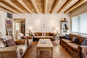 A cozy living room with wooden beams, leather sofas, a wooden coffee table, and a bookshelf with decorative items.