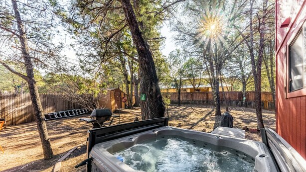 A hot tub in a backyard with trees and a wooden fence. - Mockingbird Cabin by Ruidoso Vacation Rentals (Ruidoso Downs)