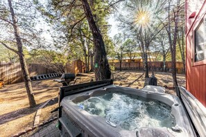 A hot tub in a backyard with trees and a wooden fence. - Mockingbird Cabin by Ruidoso Vacation Rentals (Ruidoso Downs)