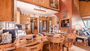 A cozy kitchen with wooden cabinets, a dining table with chairs, a refrigerator, and a TV mounted on the wall. - Mockingbird Cabin by Ruidoso Vacation Rentals (Ruidoso Downs)