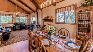 A cozy living room with a fireplace, leather sofas, and a dining area with a wooden table set for six. - Mockingbird Cabin by Ruidoso Vacation Rentals (Ruidoso Downs)