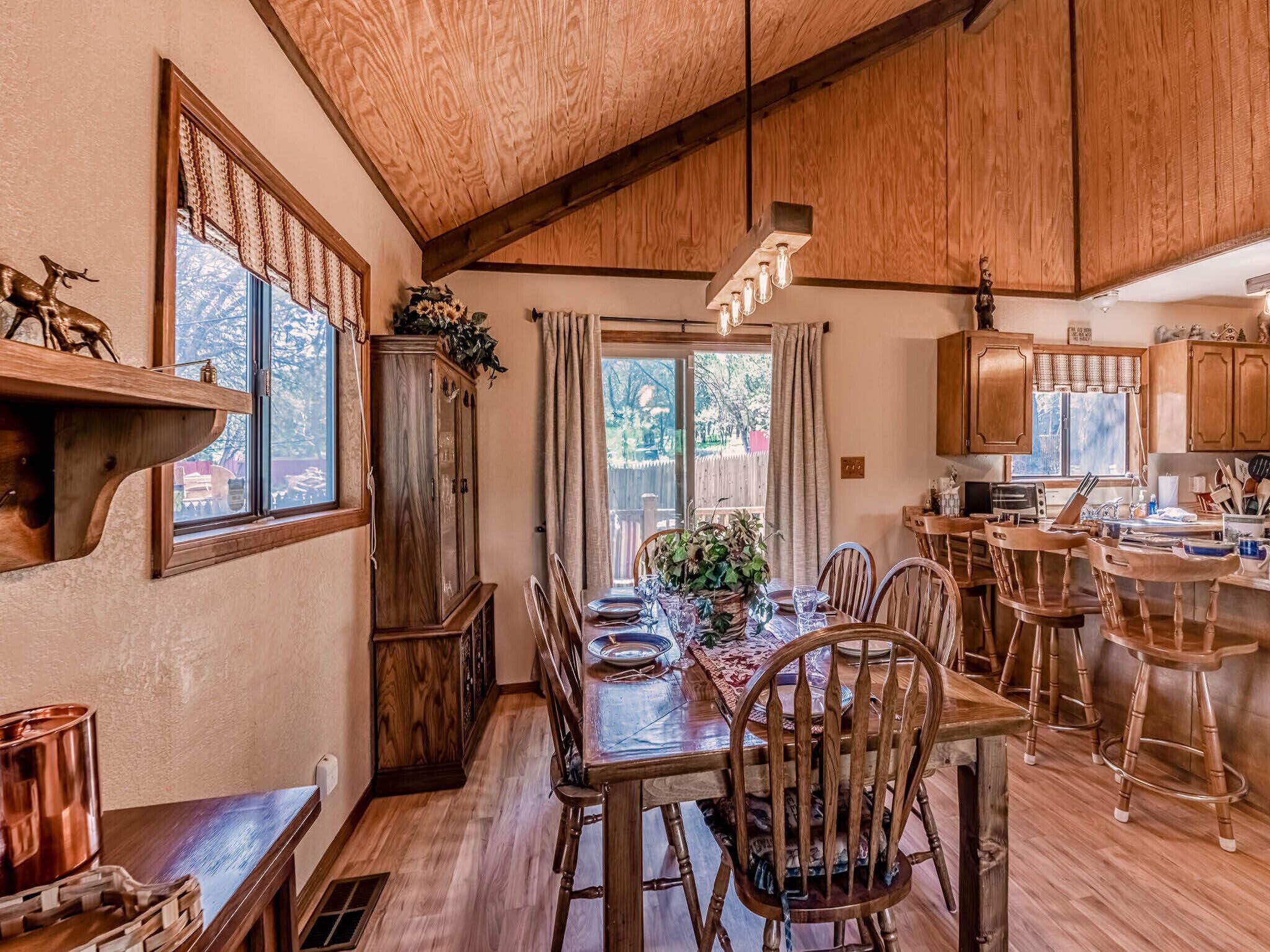 A dining area with a wooden table and chairs, a kitchen with wooden cabinets, and a window with curtains.