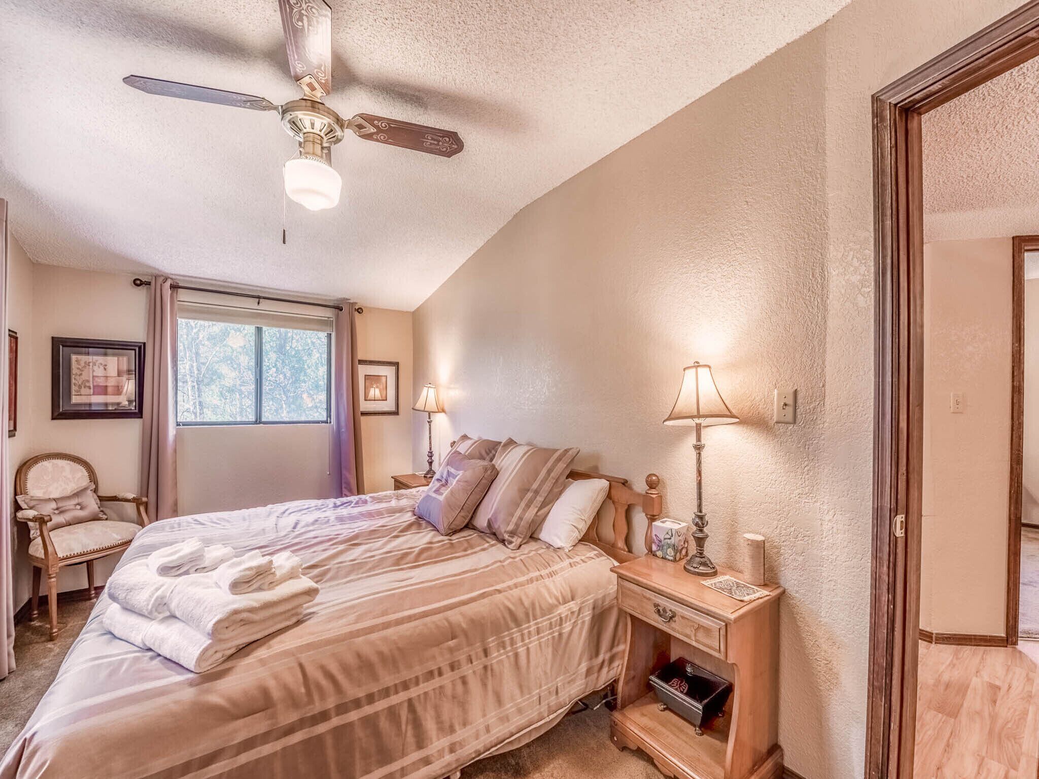 A bedroom with a bed, a nightstand, a chair, a ceiling fan, and a window.