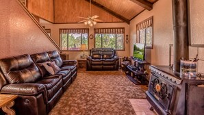 A cozy living room with a fireplace, leather sofa, and a ceiling fan. - Mockingbird Cabin by Ruidoso Vacation Rentals (Ruidoso Downs)
