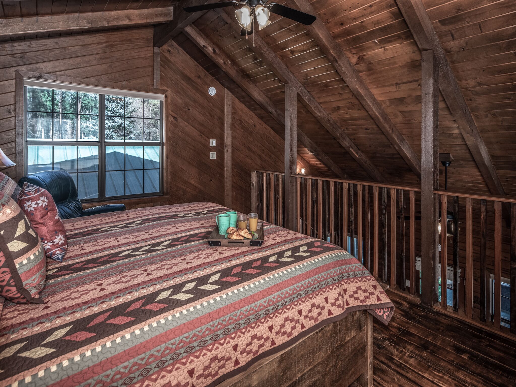 Une pièce rustique en bois, dotée d’un grand lit, d’une fenêtre et d’un ventilateur de plafond.