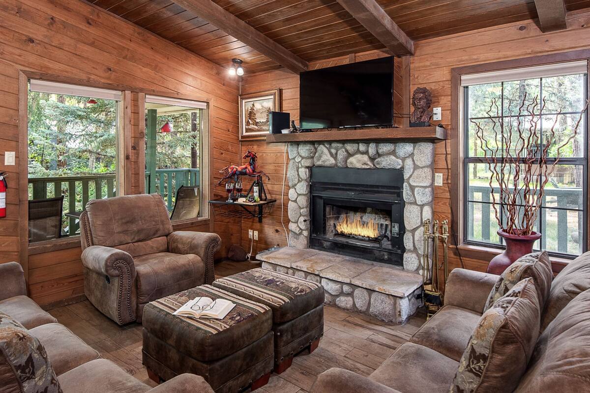 A cozy cabin interior with a stone fireplace, wooden walls, and a comfortable seating area.
