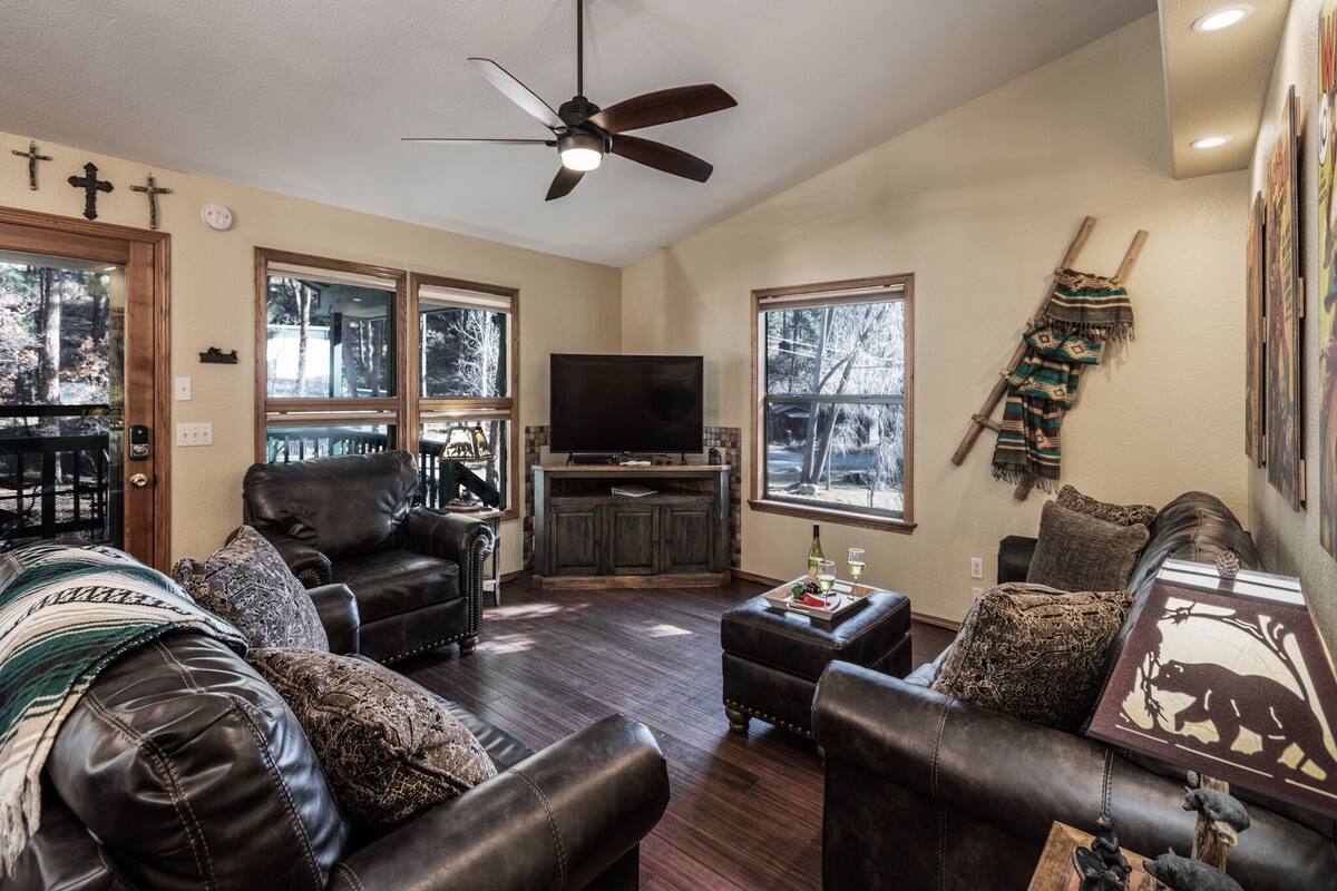 A living room with leather sofas, a ceiling fan, a TV, and large windows.
