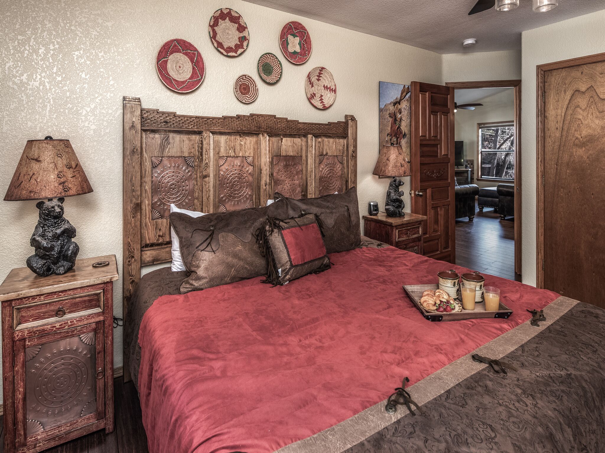 Une chambre à coucher avec une tête de lit en bois, une couvre-lit rouge et un plateau de pâtisseries sur le lit.