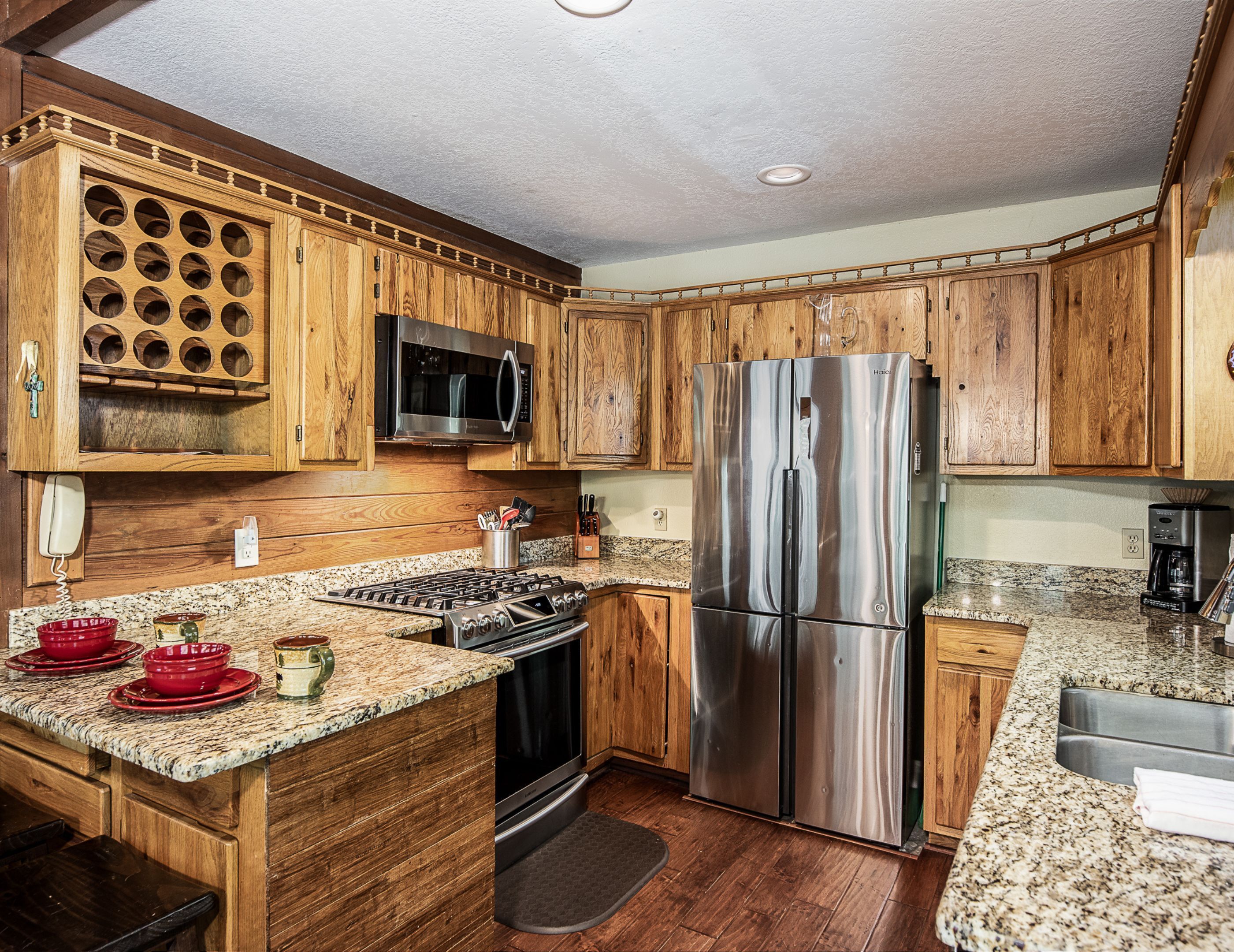 A kitchen with wooden cabinets, a stainless steel refrigerator, a microwave, and granite countertops.
