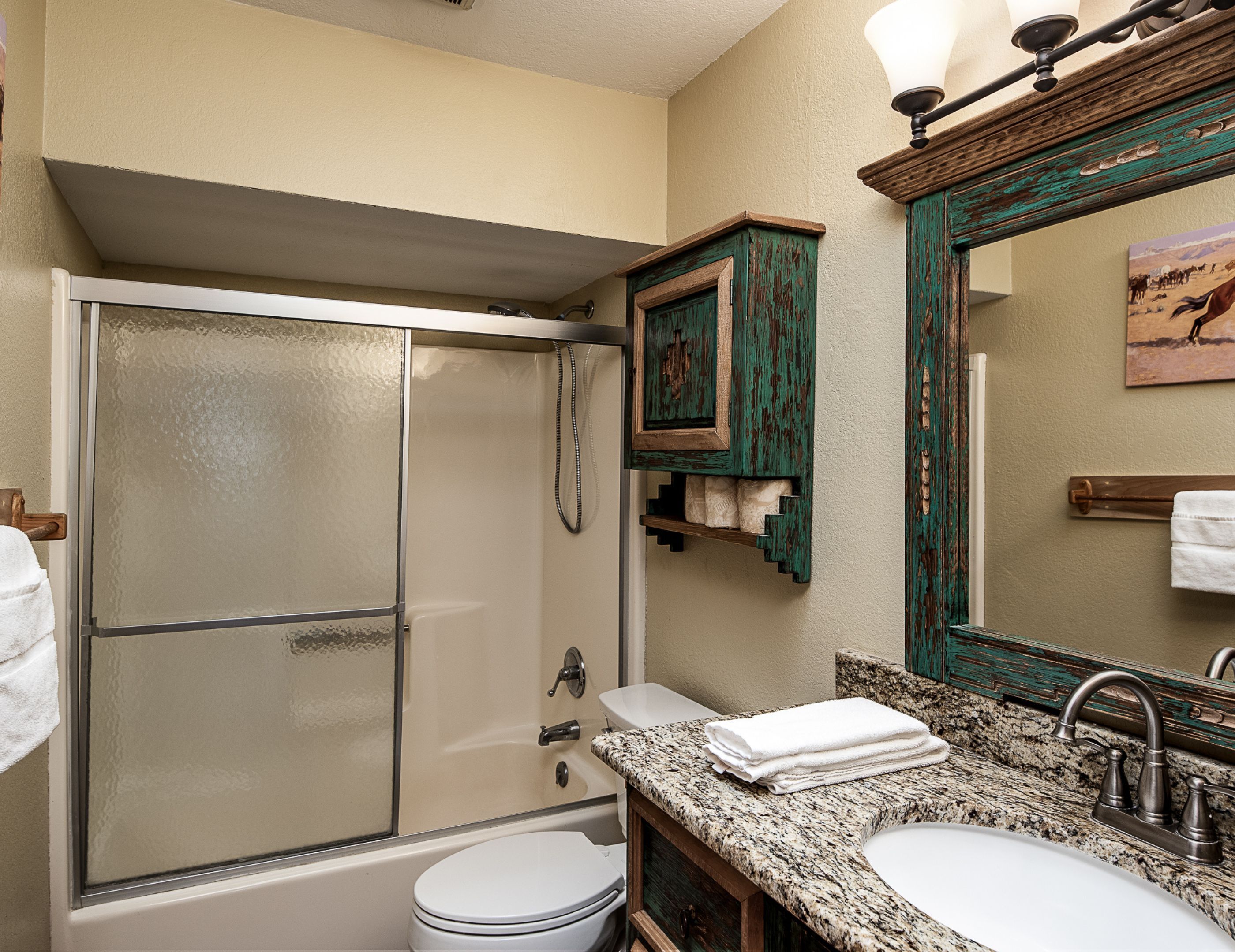 A bathroom with a glass-enclosed shower, a white toilet, a granite countertop sink, and a mirror with a decorative frame.