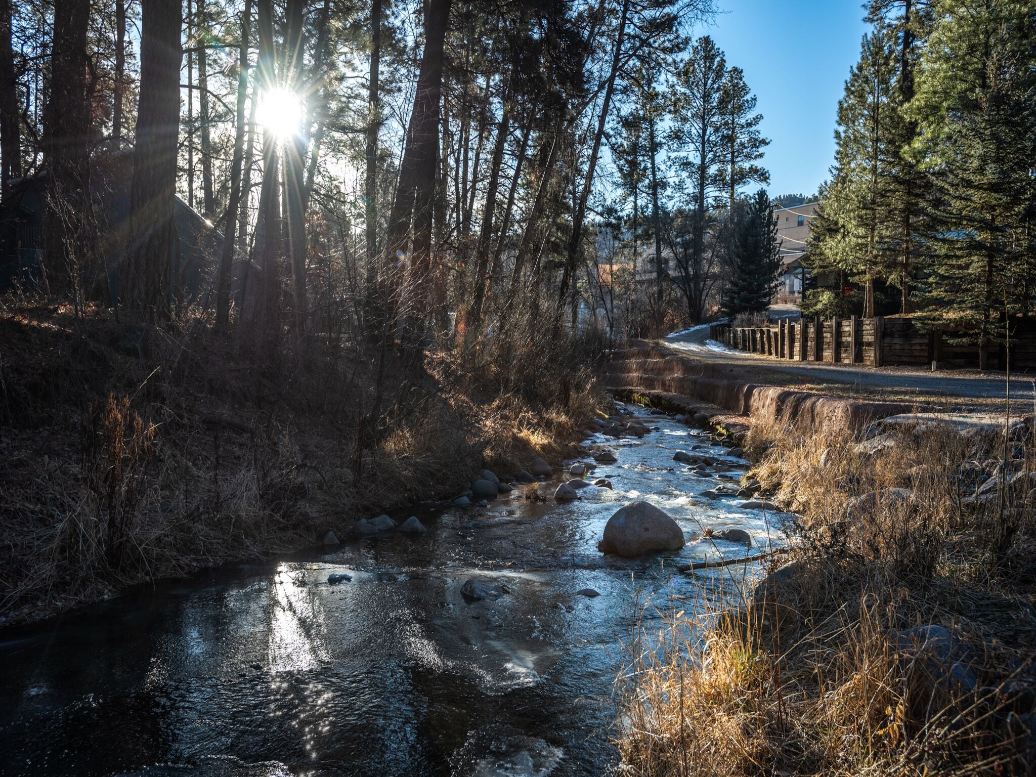 A river flowing through a forested area with a stone bridge and a building in the background.