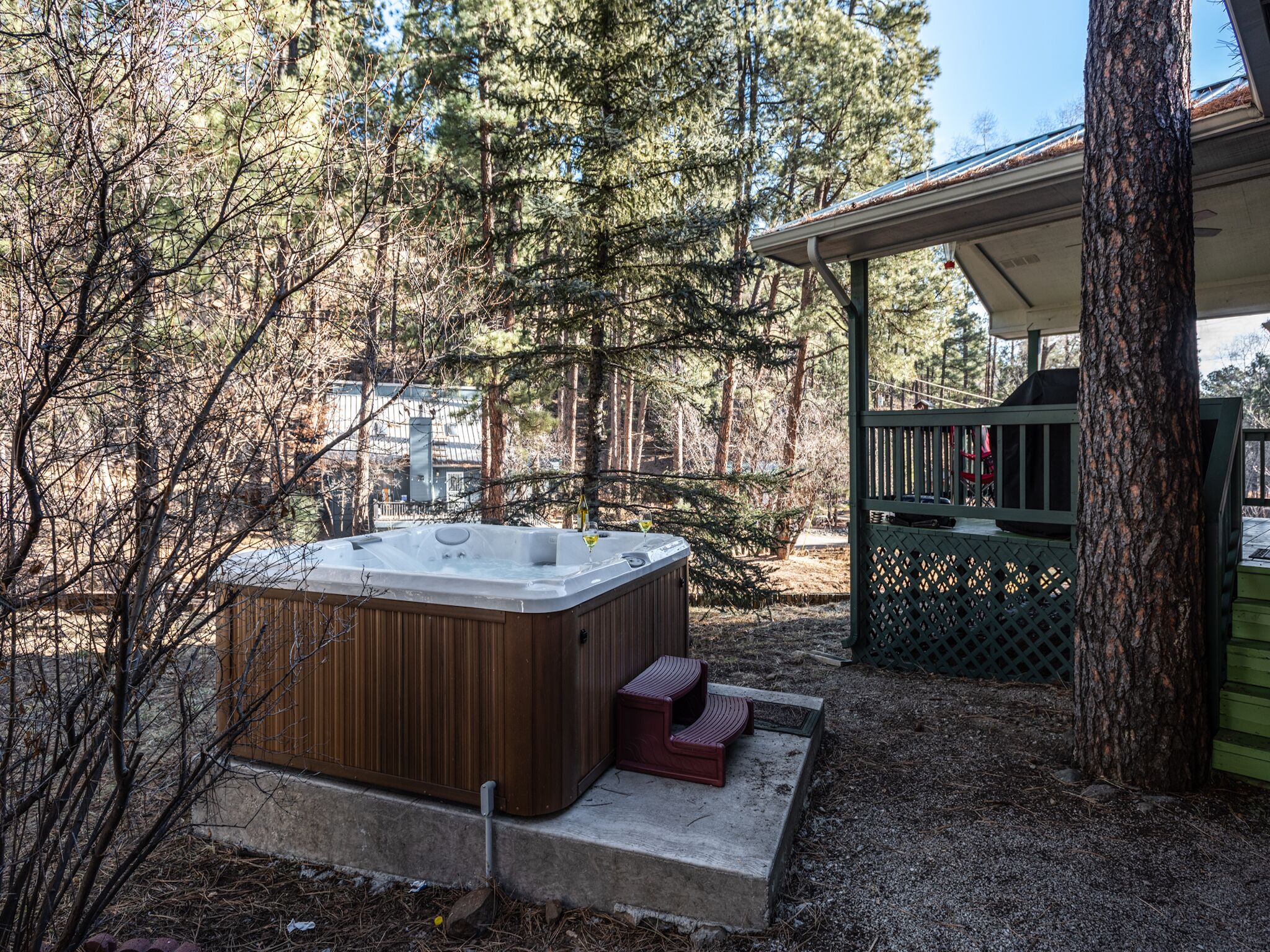 Un jacuzzi en zona boscosa con terraza cubierta y escalones de acceso.