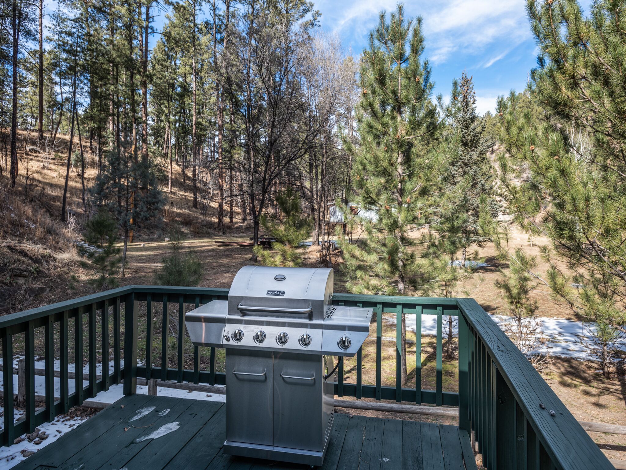 Una parrilla en una terraza de madera con vistas a un bosque y un río.