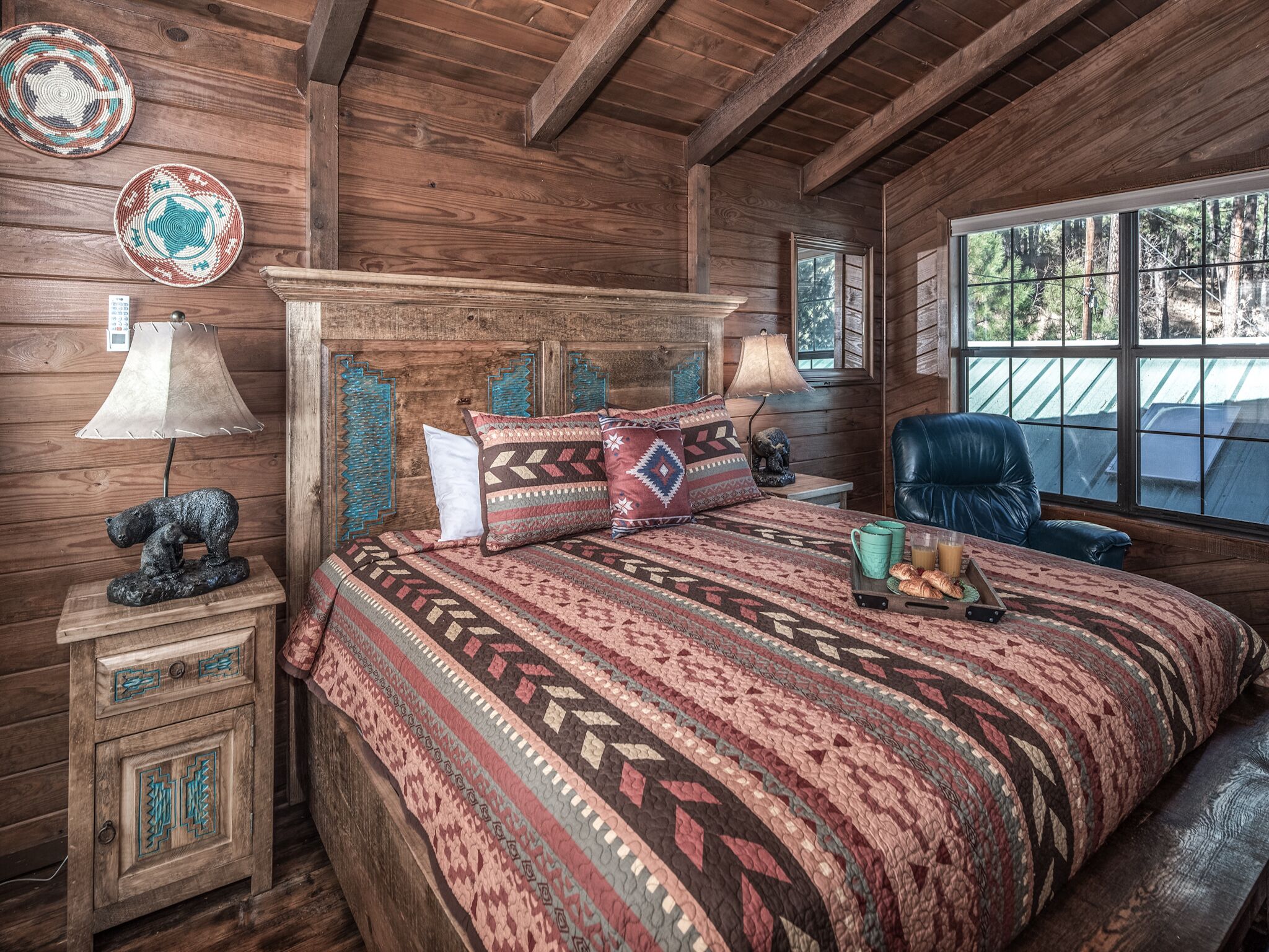 A rustic wooden bedroom with a large bed, a chair, and a window with a forest view.