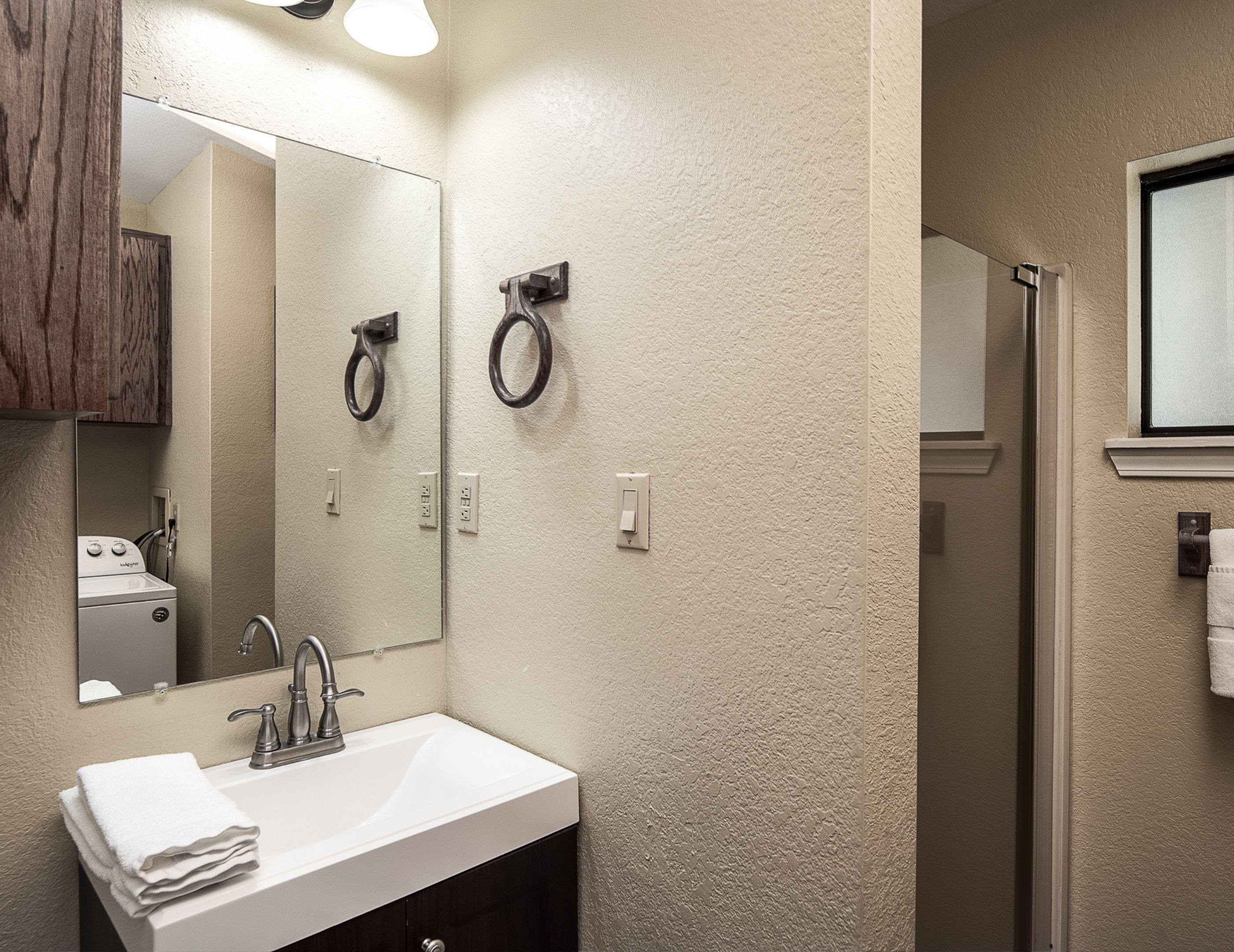 A bathroom with a sink, mirror, towel rack, and a shower area.