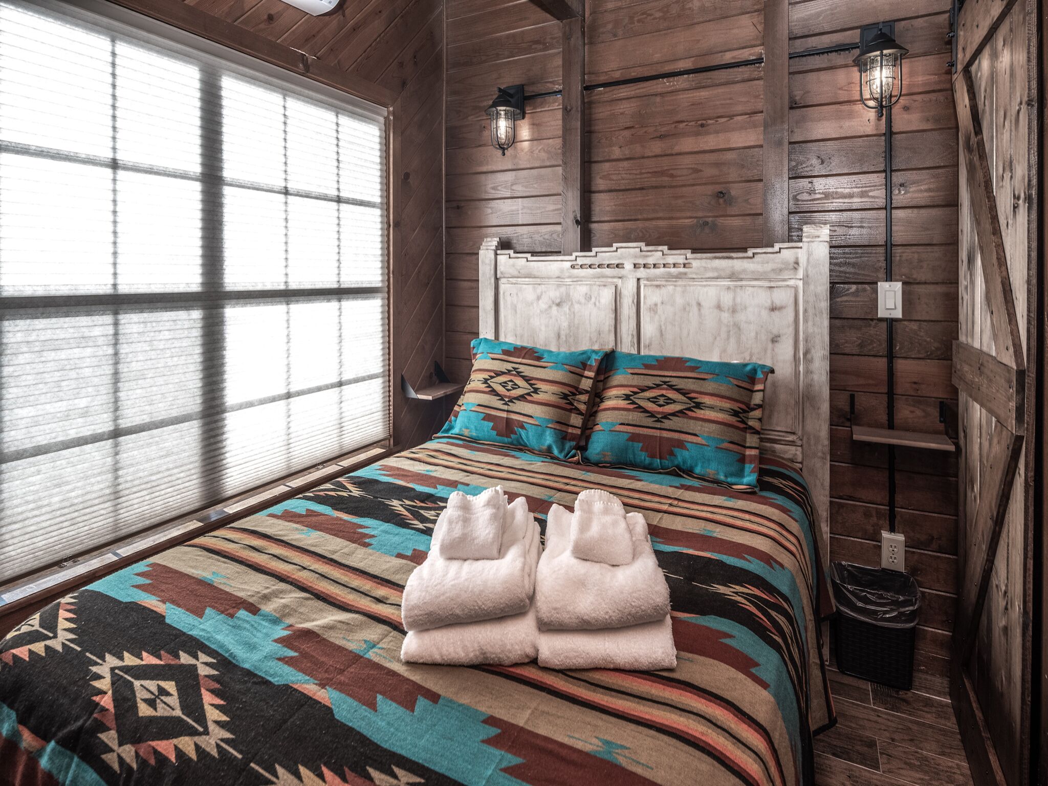 Un dormitorio de cabaña de madera con una cama, dos almohadas, un edredón y un par de toallas.