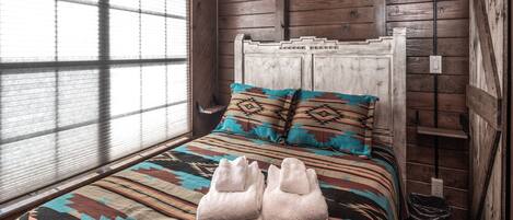 Un dormitorio de cabaña de madera con una cama, dos almohadas, un edredón y un par de toallas.