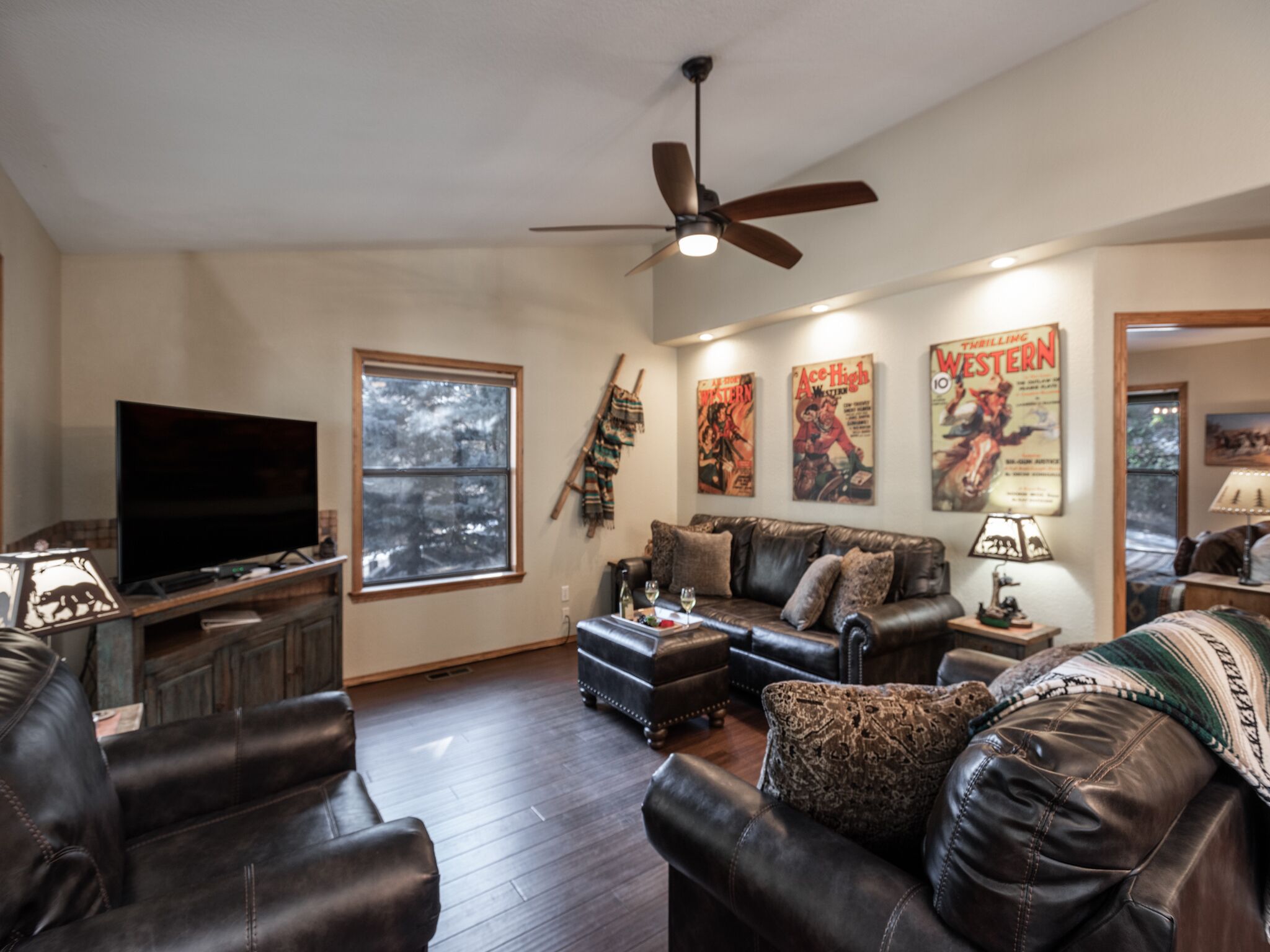 A living room with leather sofas, a television, a ceiling fan, and posters on the wall.
