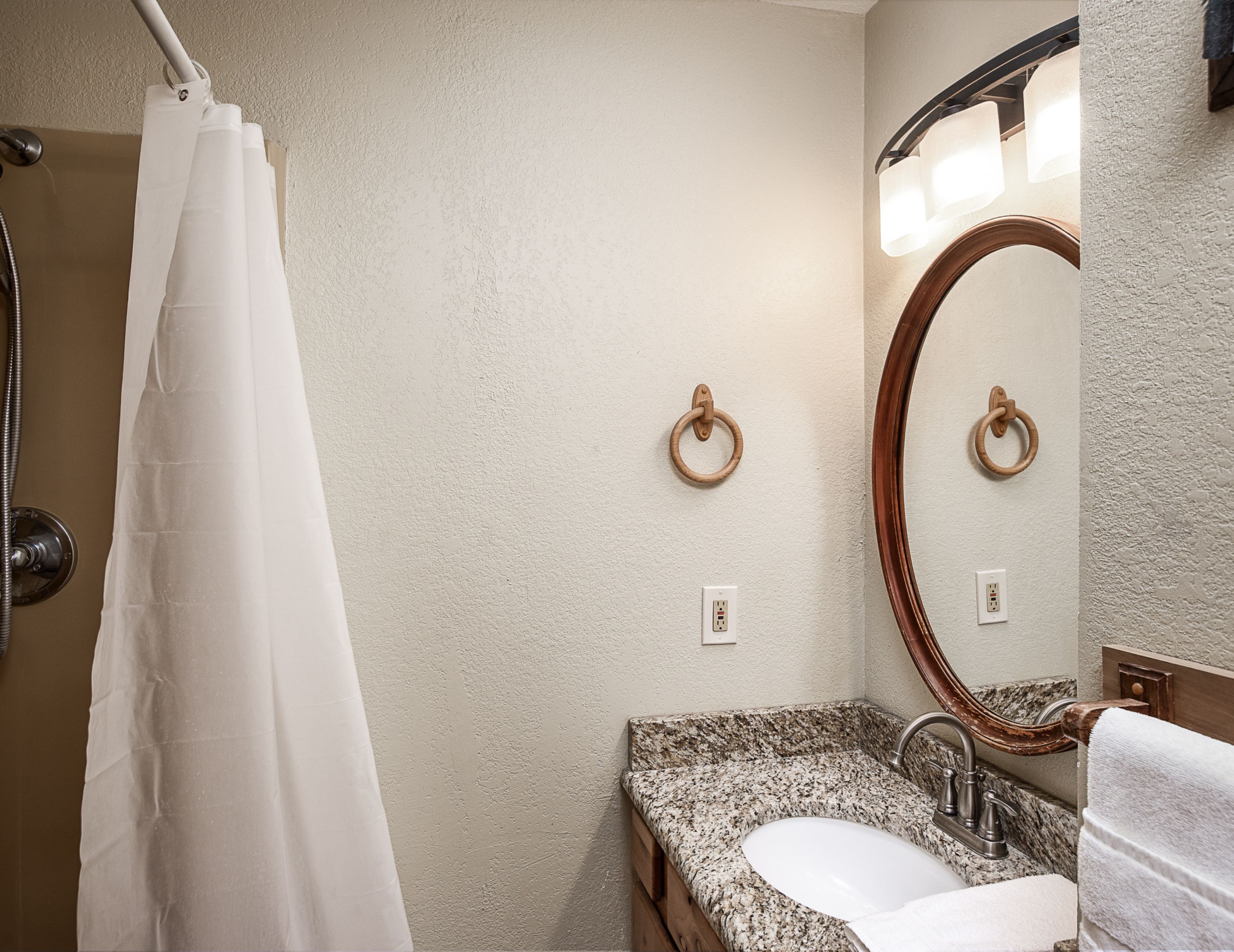 A bathroom with a shower curtain, a sink with a marble countertop, a wooden ring towel ring, and a mirror with a wooden frame.