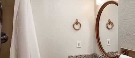 A bathroom with a shower curtain, a sink with a marble countertop, a wooden ring towel ring, and a mirror with a wooden frame.