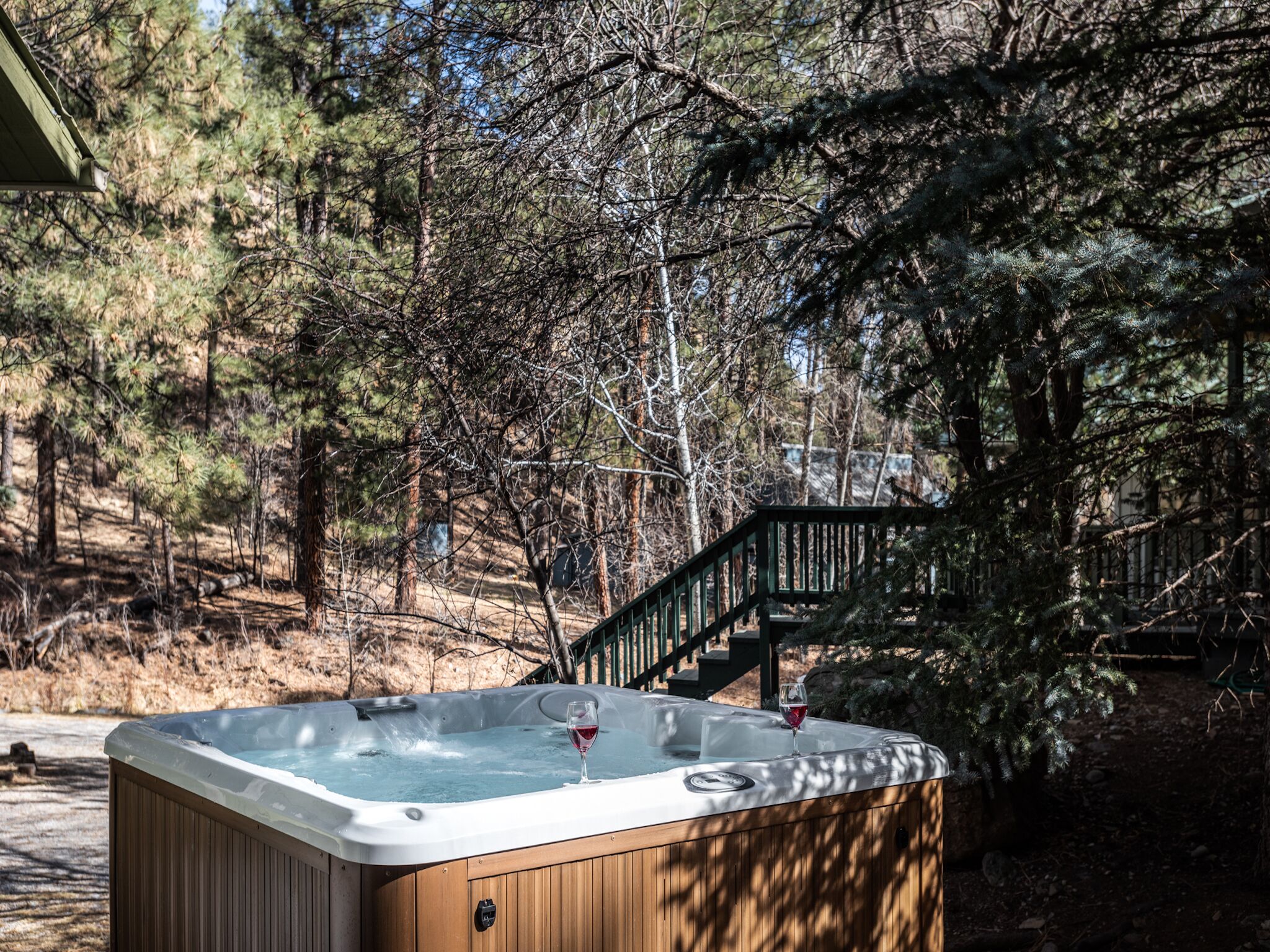 Un bain à remous situé dans une zone boisée, avec une terrasse en bois et un escalier menant à un bâtiment.