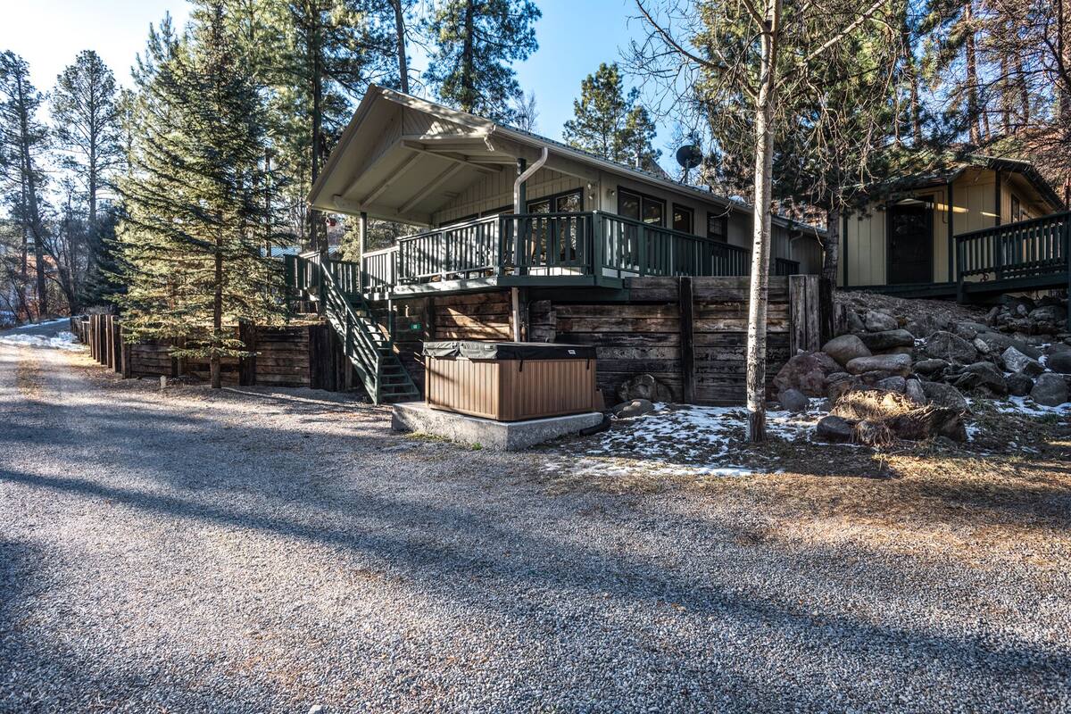 A lodge with a covered deck, a hot tub, and a stone wall.