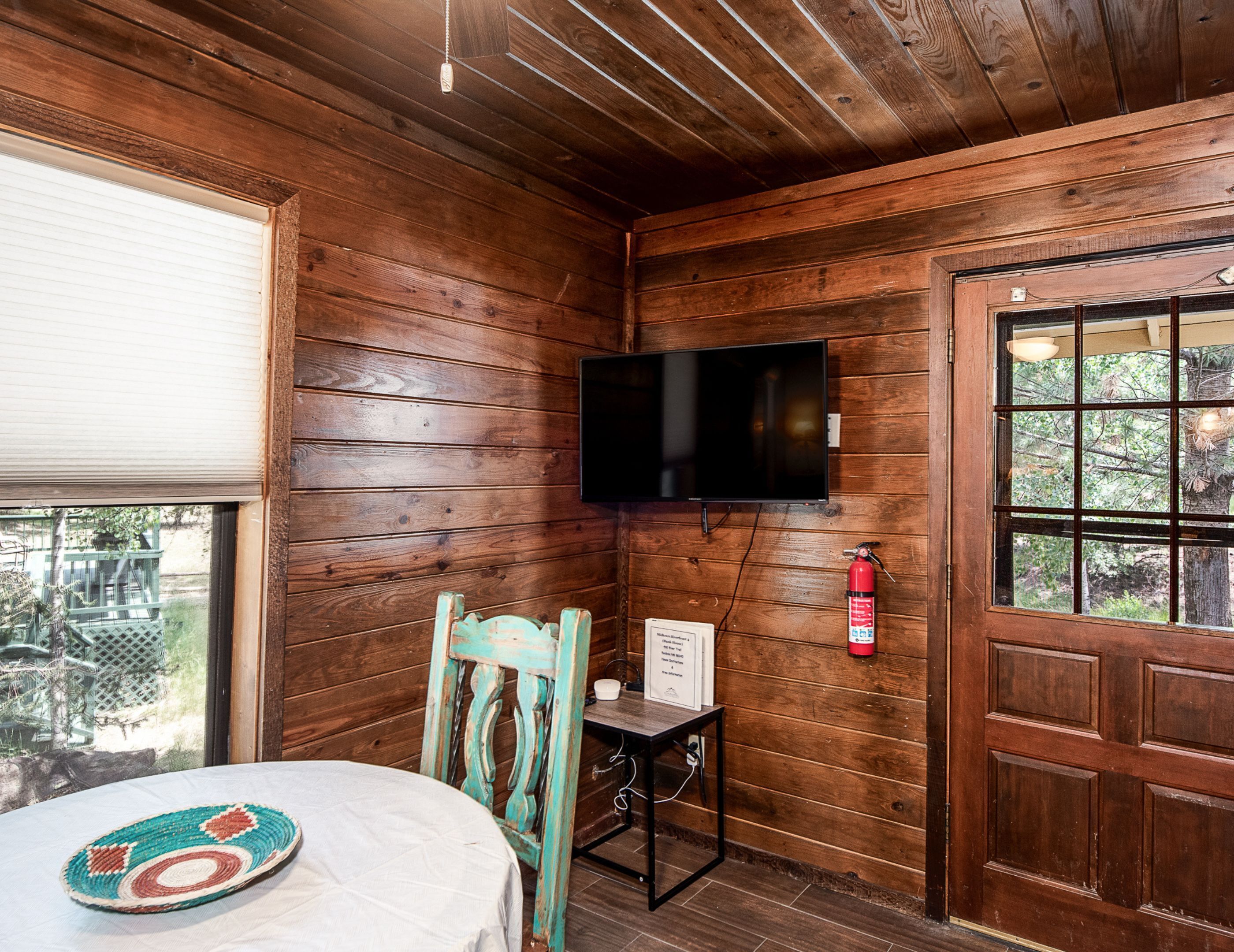A wooden cabin interior with a television mounted on the wall, a door with a window, and a table with a placemat.